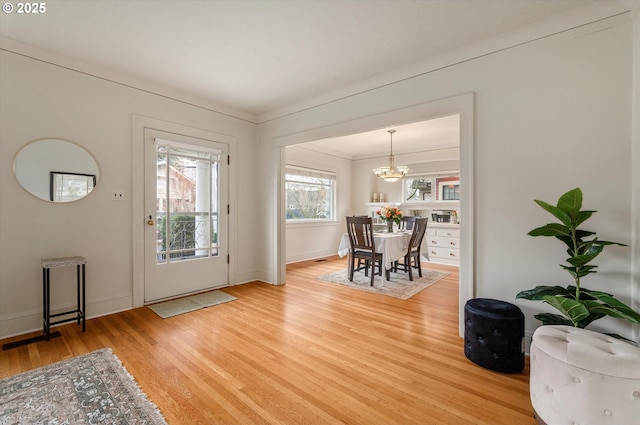 foyer entrance with visible vents, baseboards, ornamental molding, light wood-style flooring, and an inviting chandelier