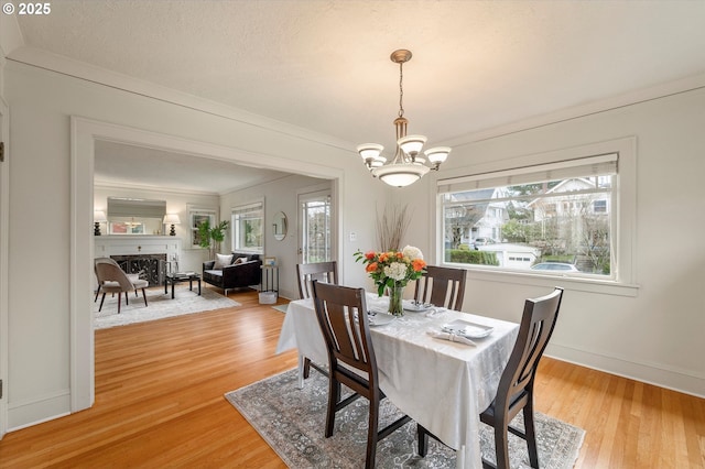 dining room featuring light wood finished floors, crown molding, baseboards, a fireplace, and an inviting chandelier