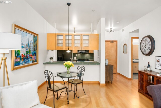 kitchen with black appliances, decorative backsplash, light brown cabinetry, kitchen peninsula, and light wood-type flooring