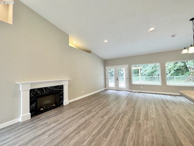 unfurnished living room featuring baseboards, a premium fireplace, french doors, wood finished floors, and high vaulted ceiling