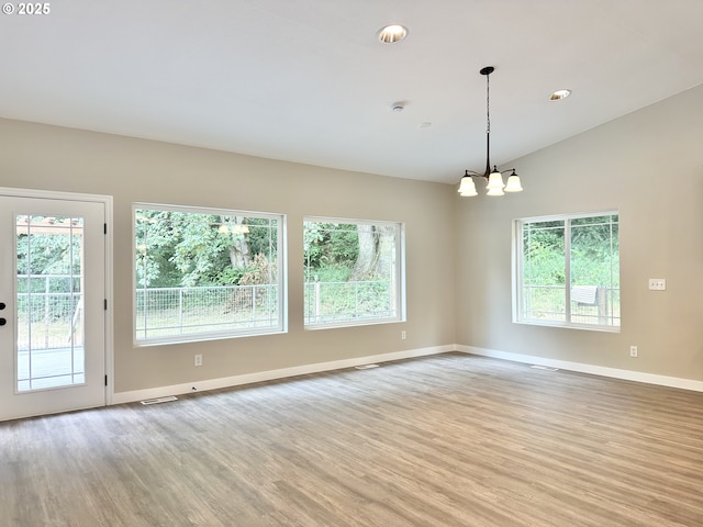 spare room with visible vents, baseboards, an inviting chandelier, light wood-style flooring, and vaulted ceiling