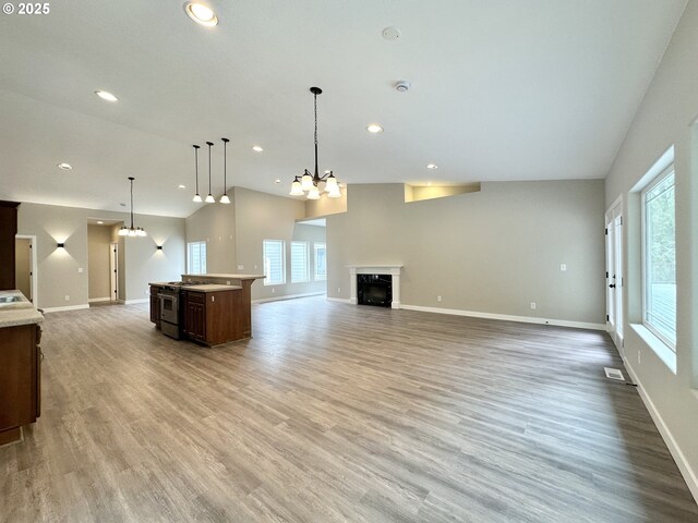 unfurnished living room featuring visible vents, baseboards, a chandelier, light wood-style flooring, and a fireplace