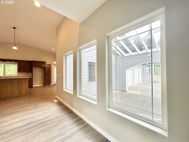 interior space with lofted ceiling, light wood-style flooring, visible vents, and baseboards