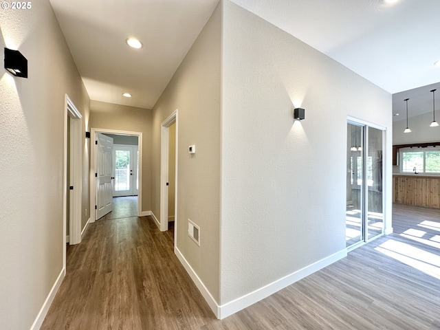 hall with wood finished floors, visible vents, and baseboards