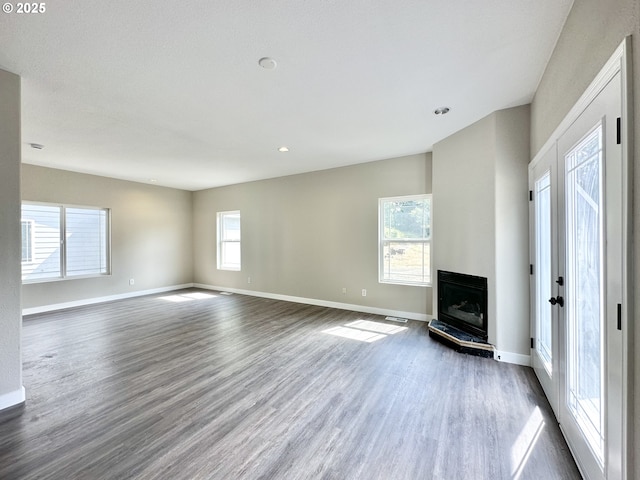 unfurnished living room featuring plenty of natural light, dark wood-type flooring, baseboards, and a glass covered fireplace