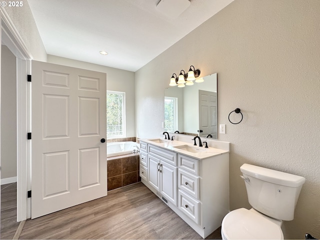 bathroom featuring a bath, toilet, wood finished floors, and a sink