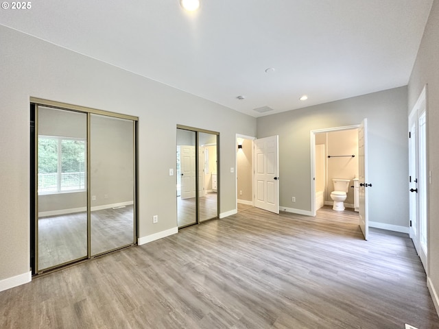 unfurnished bedroom featuring wood finished floors, baseboards, and two closets