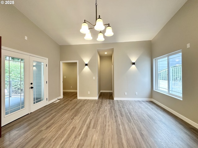 empty room featuring wood finished floors, baseboards, an inviting chandelier, vaulted ceiling, and french doors