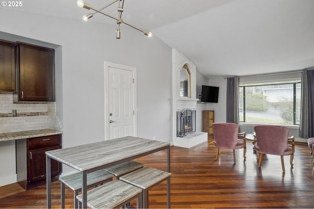 dining room with a brick fireplace, vaulted ceiling, dark hardwood / wood-style floors, and a chandelier