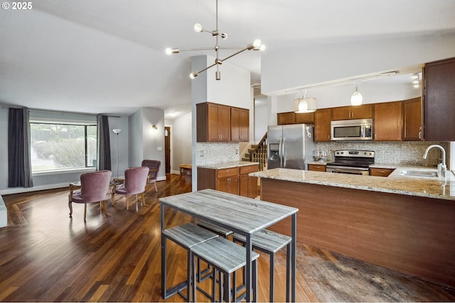 kitchen with dark wood-type flooring, sink, decorative light fixtures, appliances with stainless steel finishes, and light stone countertops