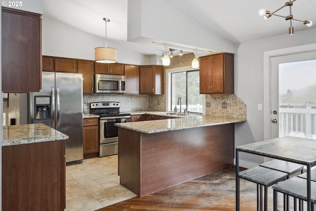 kitchen with appliances with stainless steel finishes, decorative light fixtures, lofted ceiling, sink, and kitchen peninsula