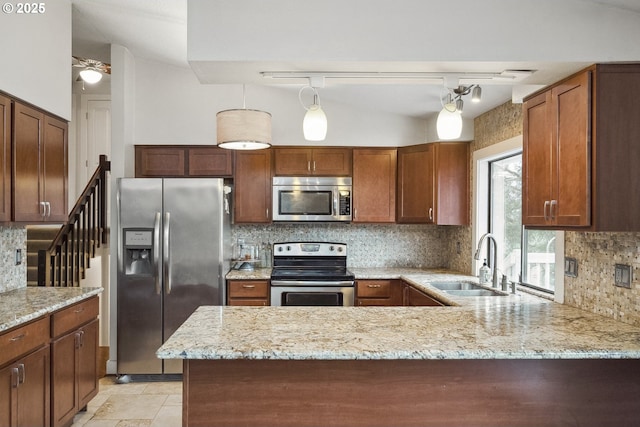 kitchen featuring stainless steel appliances, sink, light stone counters, and kitchen peninsula