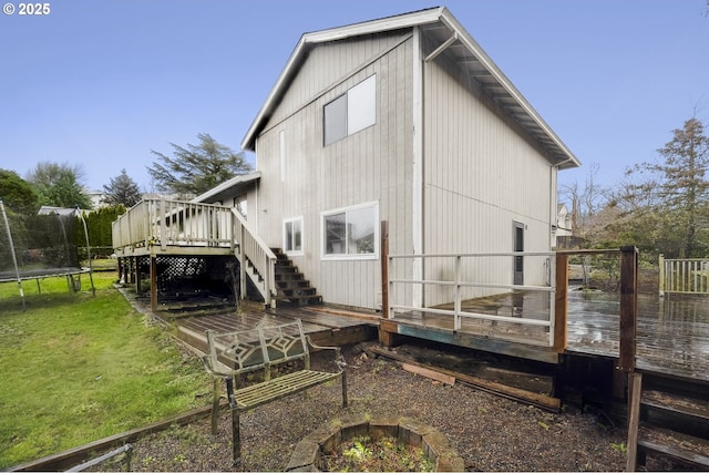 rear view of property with a deck, a fire pit, a trampoline, and a lawn