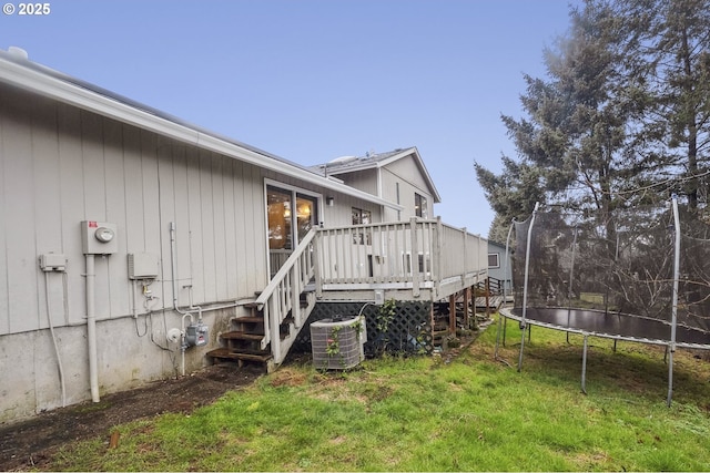 view of side of property featuring a wooden deck, a yard, a trampoline, and central air condition unit