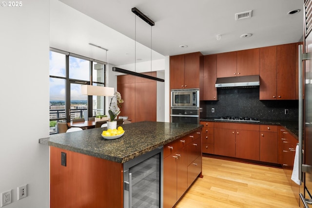 1025 NW Couch St Unit 1320, Portland, OR 97209 - kitchen with wine cooler, appliances with stainless steel finishes, under cabinet range hood, tasteful backsplash, and light wood finished floors