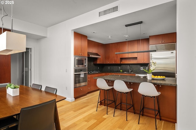 1025 NW Couch St Unit 1320, Portland, OR 97209 - kitchen featuring built in appliances, under cabinet range hood, light wood finished floors, tasteful backsplash, and a kitchen breakfast bar