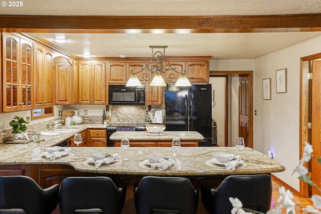 kitchen with a breakfast bar area, pendant lighting, light stone counters, and black appliances