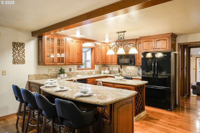 kitchen with black appliances, decorative backsplash, light hardwood / wood-style floors, hanging light fixtures, and kitchen peninsula