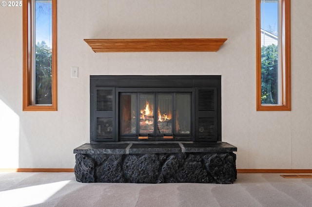 room details with a glass covered fireplace, carpet flooring, visible vents, and baseboards