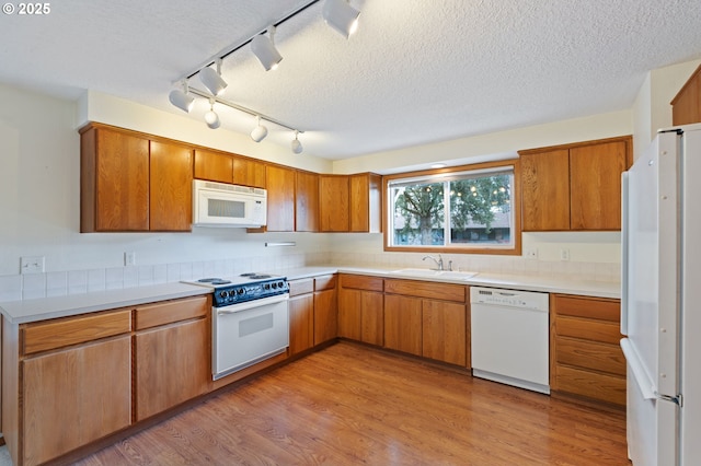 kitchen featuring brown cabinets, white appliances, light wood-style floors, and a sink