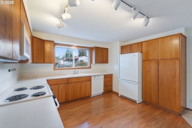 kitchen featuring a sink, white appliances, light wood-style floors, brown cabinetry, and light countertops