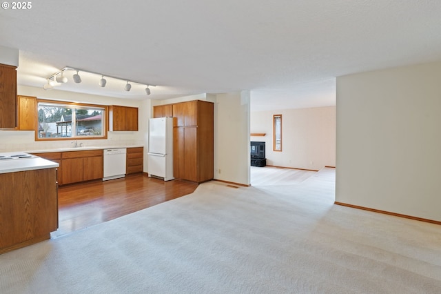 kitchen featuring light carpet, a sink, white appliances, brown cabinetry, and light countertops