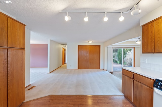 kitchen with visible vents, a textured ceiling, brown cabinetry, light countertops, and range