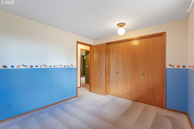 unfurnished bedroom with a closet, carpet flooring, a textured ceiling, and baseboards