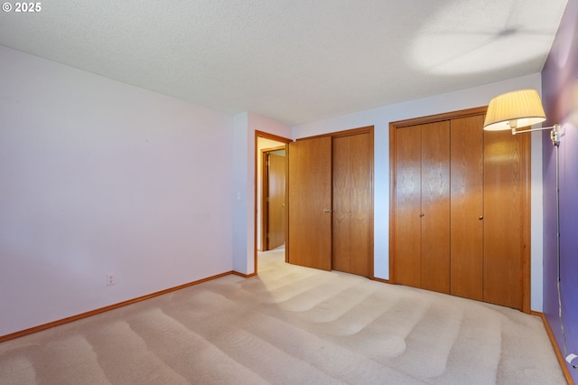 unfurnished bedroom with baseboards, a textured ceiling, two closets, and carpet