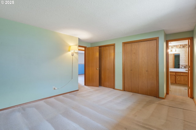 unfurnished bedroom featuring light colored carpet, a textured ceiling, two closets, and baseboards