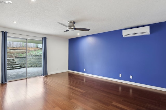 empty room with a textured ceiling, wood finished floors, a wall unit AC, baseboards, and ceiling fan