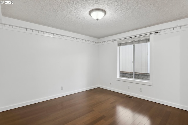 spare room featuring dark wood-style floors, visible vents, a textured ceiling, and baseboards