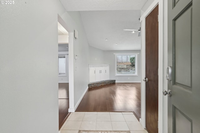 hallway with light tile patterned flooring, baseboards, and a textured ceiling