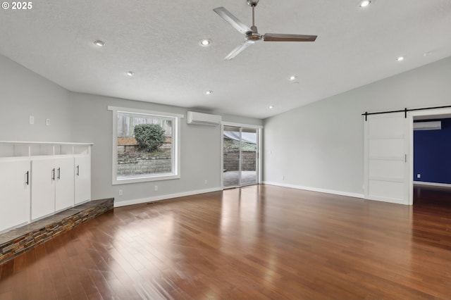 unfurnished living room with ceiling fan, a wall mounted air conditioner, a barn door, vaulted ceiling, and wood finished floors