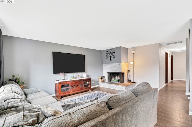 living room featuring visible vents, baseboards, a brick fireplace, and wood finished floors