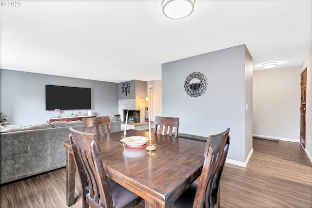 dining space with baseboards, wood finished floors, and a fireplace with raised hearth