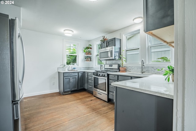 kitchen featuring appliances with stainless steel finishes, light stone counters, gray cabinetry, sink, and light hardwood / wood-style floors