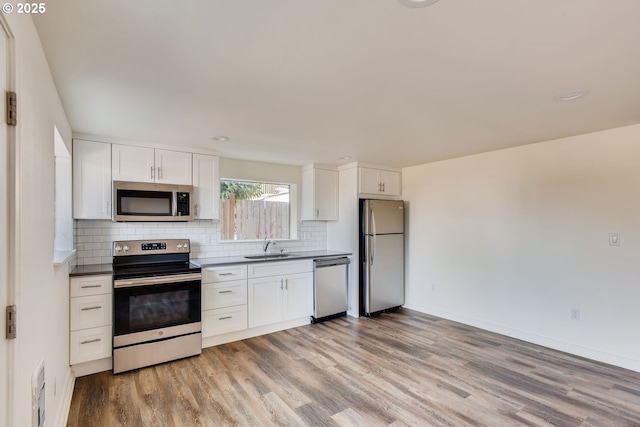 2747 NE Bryant St, Portland, OR 97211 - kitchen featuring stainless steel appliances, light wood-style flooring, backsplash, white cabinets, and dark countertops