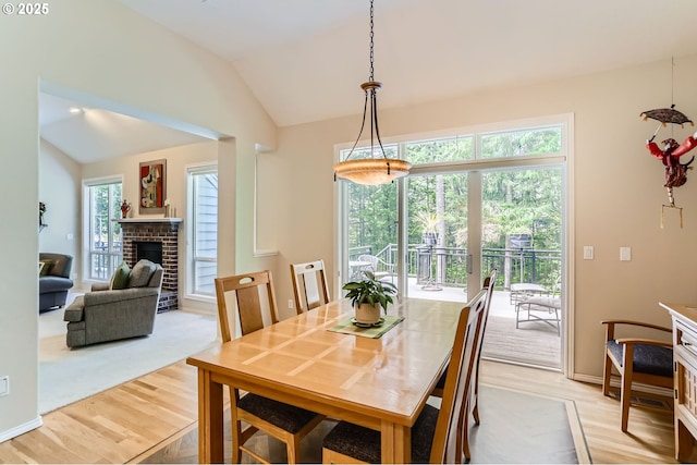 dining room featuring baseboards, a fireplace, vaulted ceiling, and light wood finished floors