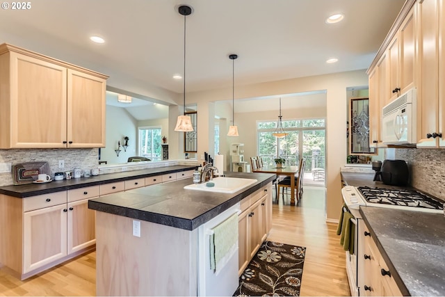 kitchen featuring light brown cabinets, dark countertops, white appliances, light wood-style floors, and a sink