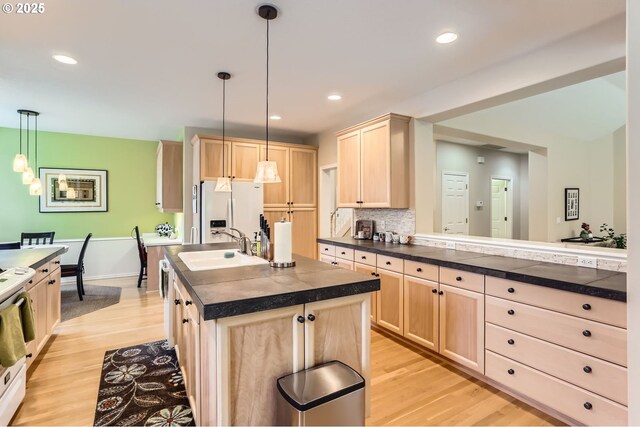 kitchen with dark countertops, light brown cabinetry, light wood-type flooring, and white appliances