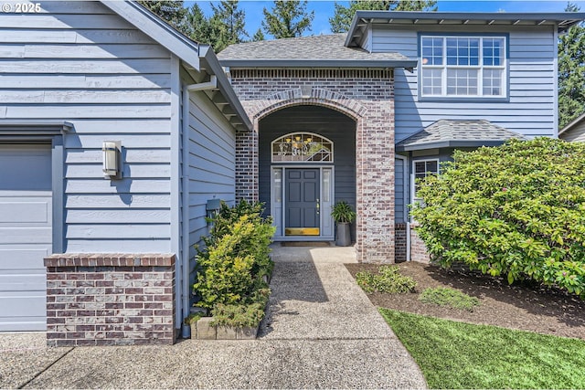view of exterior entry with brick siding and a shingled roof