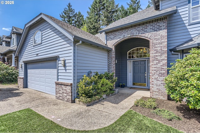 entrance to property with brick siding, driveway, roof with shingles, and a garage