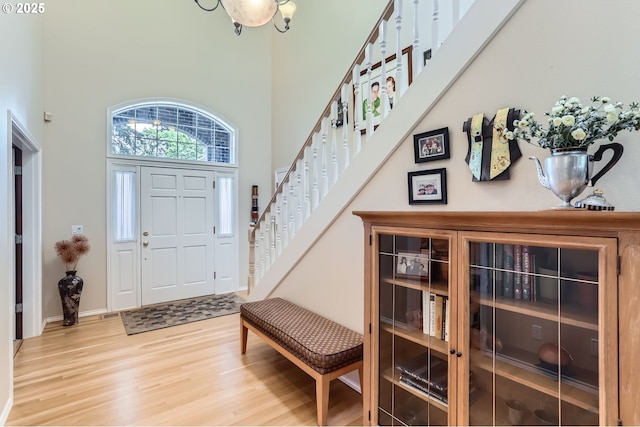 foyer with light wood-style floors, baseboards, a towering ceiling, and stairway