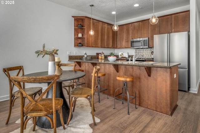 4409 NE Killingsworth St Unit 103, Portland, OR 97218 - kitchen featuring appliances with stainless steel finishes, dark stone counters, a peninsula, open shelves, and wood finished floors