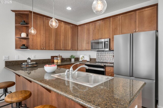 4409 NE Killingsworth St Unit 103, Portland, OR 97218 - kitchen featuring appliances with stainless steel finishes, brown cabinetry, open shelves, decorative light fixtures, and a textured ceiling