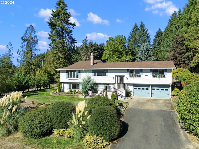 raised ranch featuring a garage, concrete driveway, and a chimney