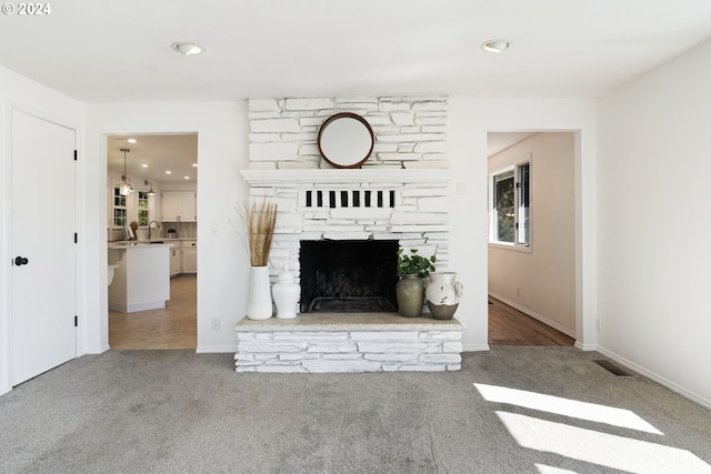 unfurnished living room featuring carpet, recessed lighting, visible vents, a sink, and a stone fireplace