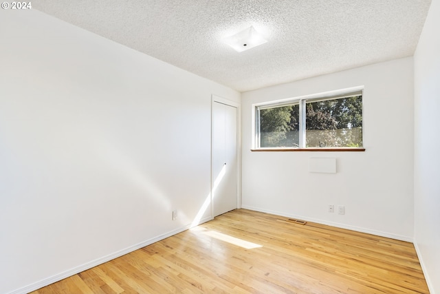 spare room with visible vents, a textured ceiling, baseboards, and wood finished floors