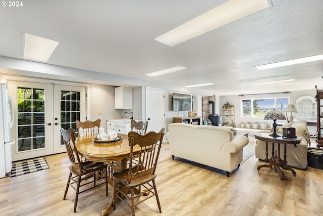 dining room with a wood stove, light wood-style floors, a textured ceiling, and french doors